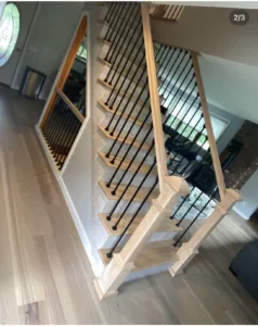 Wooden staircase with black metal balusters and a modern handrail design.