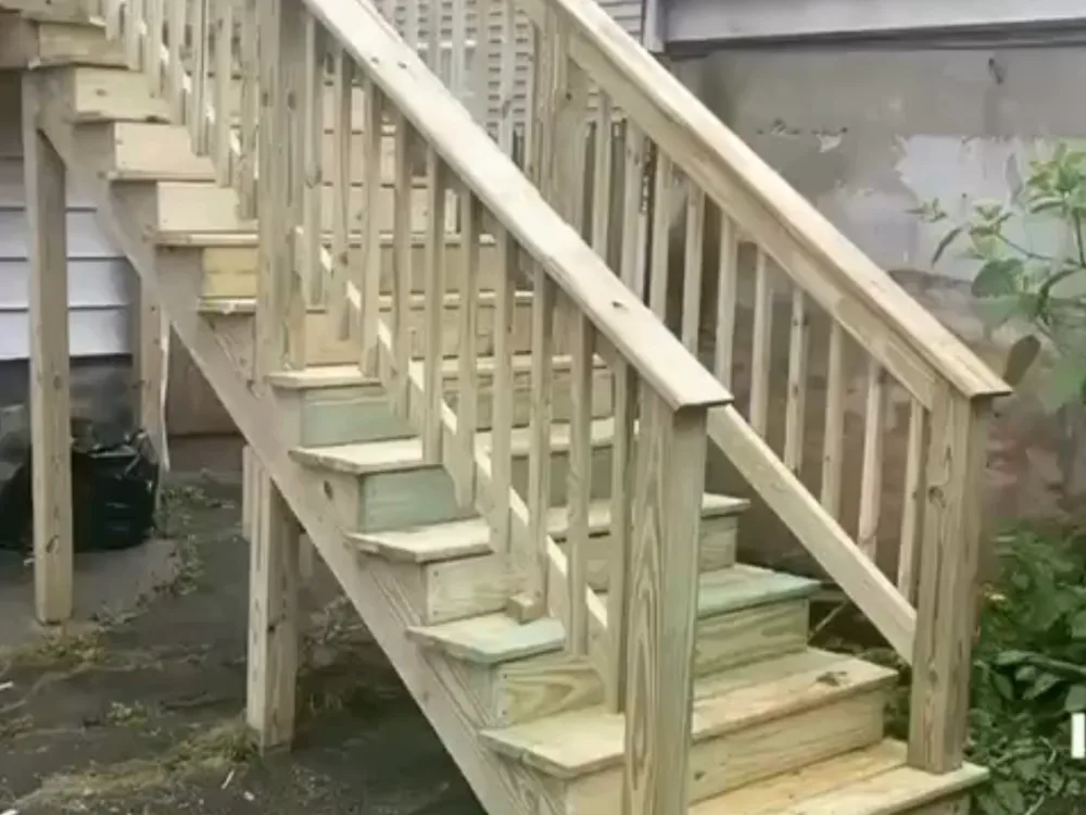 Exterior wooden staircase construction with pressure-treated lumber and safety railings for residential access